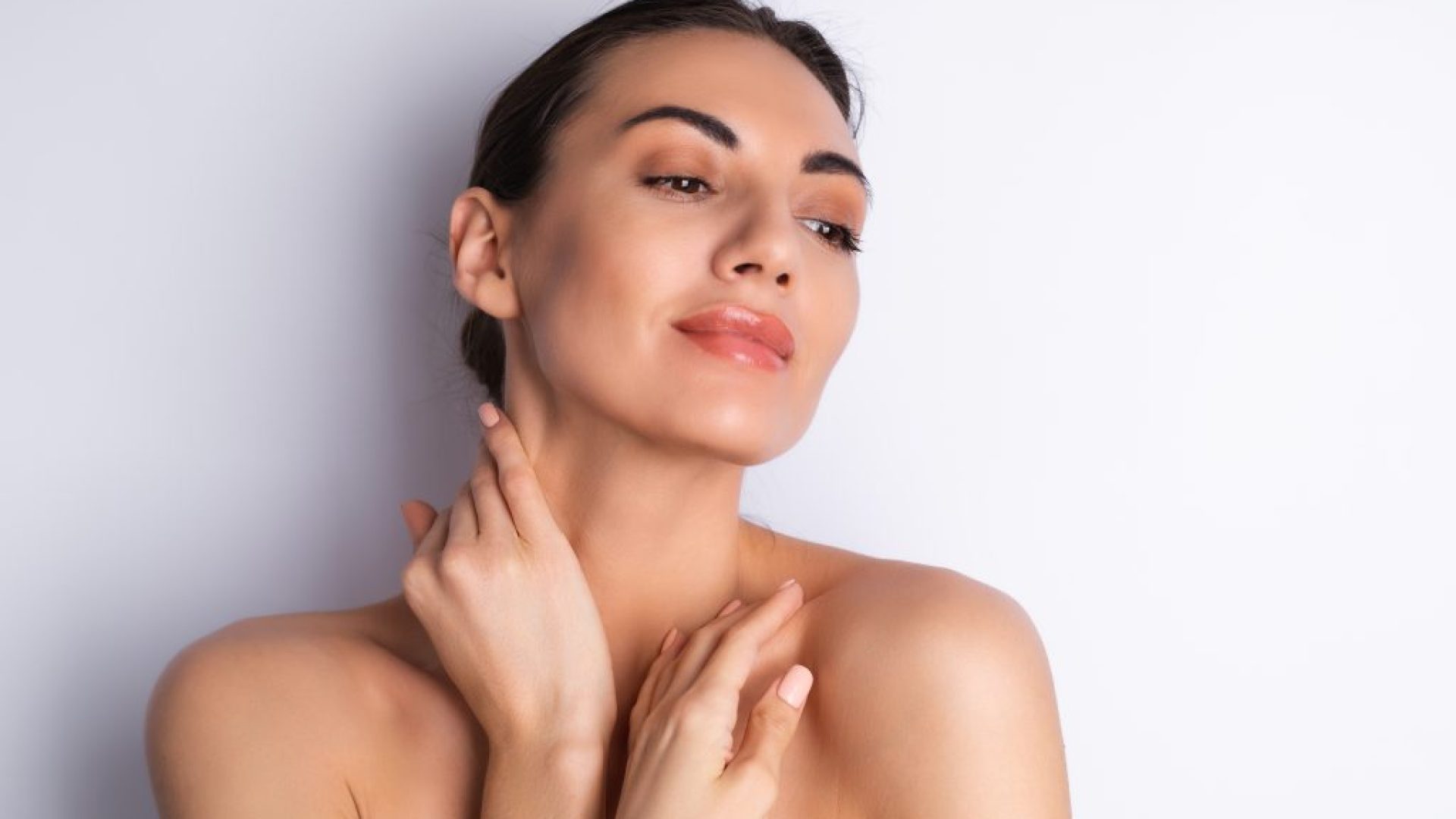 Close beauty portrait of a topless woman with perfect skin and natural make-up, plump nude lips, on a white background